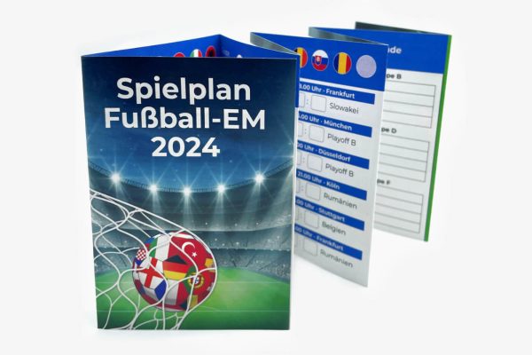 Ein Faltplan mit dem Spielplan der Fußball-EM 2024 steht auf einer hellen Unterlage aufgefächert. Eine Werbefläche ist auf dem Spielpan markiert.