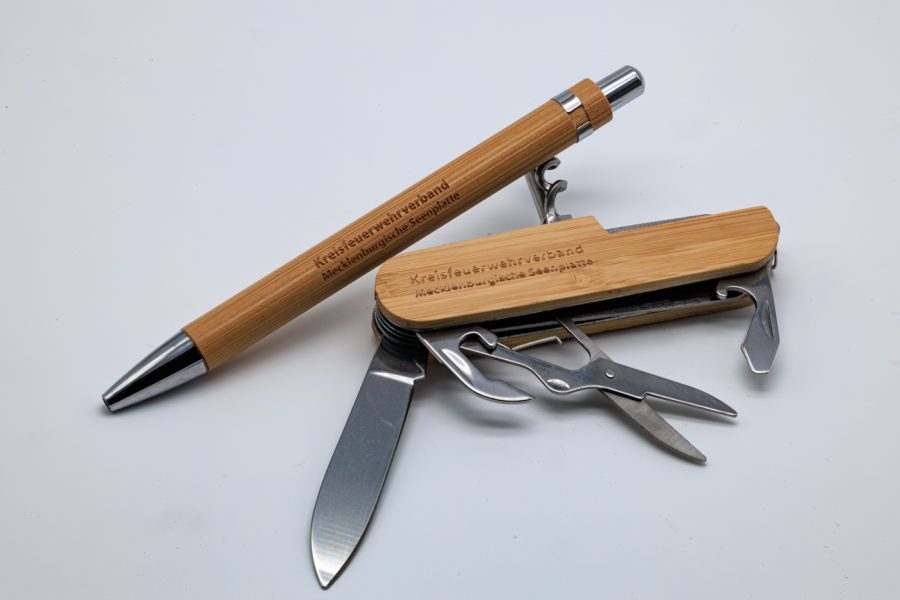 Ein Taschenmesser mit ausgeklappten Messer und anderen Funktionen. Daneben liegt ein Kugelschreiber.