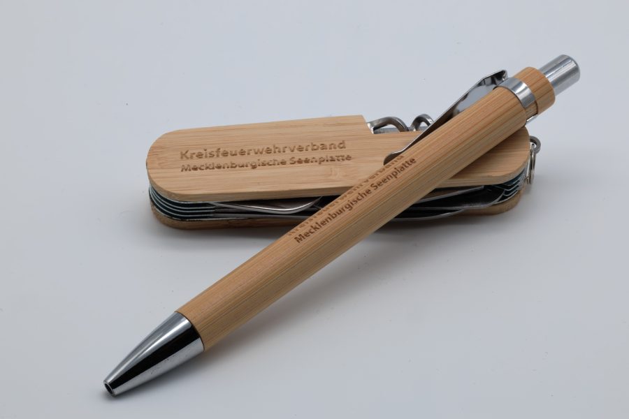 Foto eines Kugelschreibers mit Gravur im Bambusgehäuse neben einem Taschenmesser mit Bambusgehäuse